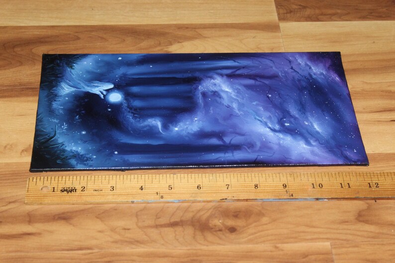 May include: A rectangular canvas painting featuring a dark blue and purple cosmic nebula scene with a glowing white orb and ethereal wisps. A wooden ruler placed along the bottom edge shows the painting is approximately 12 inches in length.