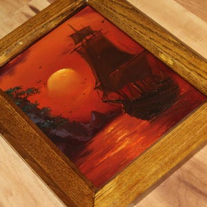 Pu&ograve; includere: Un dipinto a olio incorniciato che mostra la sagoma scura di un veliero su uno sfondo rosso e arancione vibrante con un grande sole, inserito in una cornice di legno marrone medio testurizzata con venature visibili e angoli smussati.