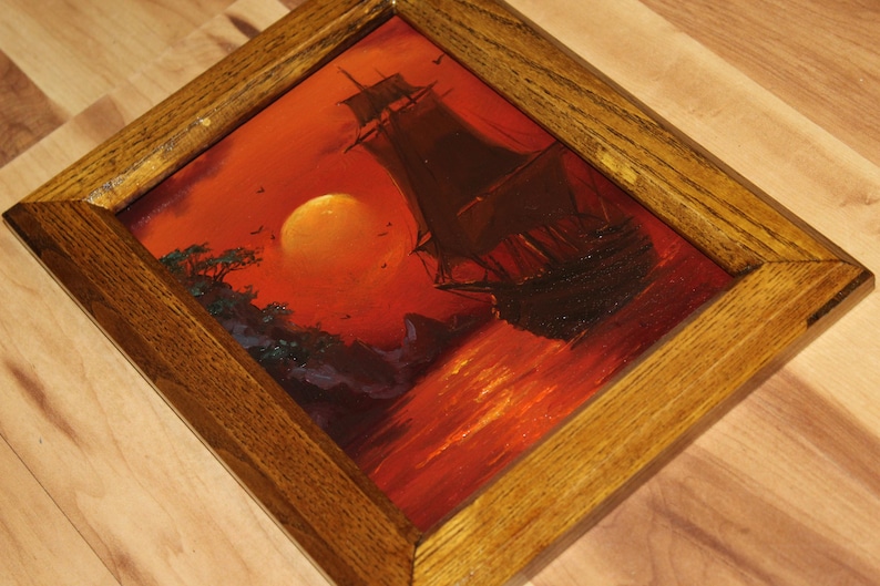 Pu&ograve; includere: Un dipinto a olio incorniciato che mostra la sagoma scura di un veliero su uno sfondo rosso e arancione vibrante con un grande sole, inserito in una cornice di legno marrone medio testurizzata con venature visibili e angoli smussati.