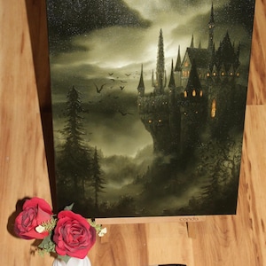 May include: A canvas print of a gothic castle at night, with a dark, moody color palette. The artwork features a detailed depiction of the castle with multiple spires, set against a cloudy sky. A small vase of red roses and a black marker are in the foreground.
