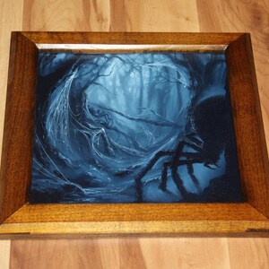 May include: A square wooden frame containing a dark blue and black painting of a forest scene. The artwork depicts a large spider with long legs in the foreground, set against a backdrop of dense, misty trees draped in intricate spider webs.