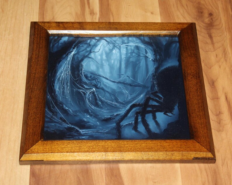 May include: A square wooden frame containing a dark blue and black painting of a forest scene. The artwork depicts a large spider with long legs in the foreground, set against a backdrop of dense, misty trees draped in intricate spider webs.