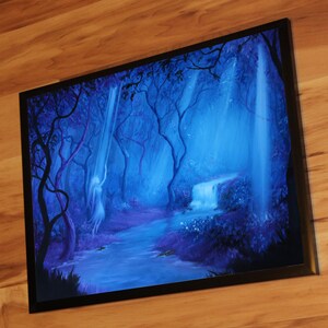 May include: Framed artwork depicting a mystical forest scene. The painting features a waterfall, a flowing river, and silhouetted trees in shades of blue and purple. A ghostly figure is visible near the waterfall. The artwork is framed in a black border.