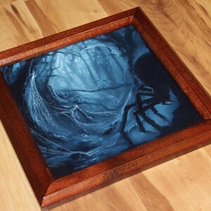 May include: A square wooden frame containing a dark blue and black painting of a forest scene with a large spider silhouette on the right side. The artwork features intricate web details and deep shadows, encased in a polished brown wood border.