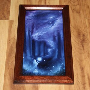 May include: A rectangular framed print featuring a dark blue forest scene with a glowing white orb held by a figure in a flowing garment. The artwork is encased in a polished dark brown wooden frame with a smooth, glossy finish and beveled edges.