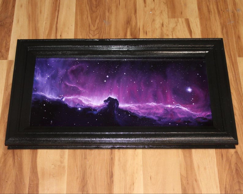 May include: A rectangular black framed art piece featuring a vibrant depiction of a nebula in shades of purple, pink, and white. The artwork showcases a celestial scene with stars and cosmic clouds, creating a dramatic and colorful display.