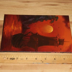 Pu&ograve; includere: Un dipinto rettangolare che presenta la sagoma scura di un veliero su uno sfondo arancione e rosso vibrante con una grande luna, posizionato accanto a un righello di legno che mostra che il dipinto &egrave; largo circa 23 cm.