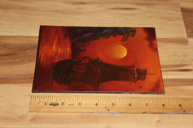 Pu&ograve; includere: Un dipinto rettangolare che presenta la sagoma scura di un veliero su uno sfondo arancione e rosso vibrante con una grande luna, posizionato accanto a un righello di legno che mostra che il dipinto &egrave; largo circa 23 cm.