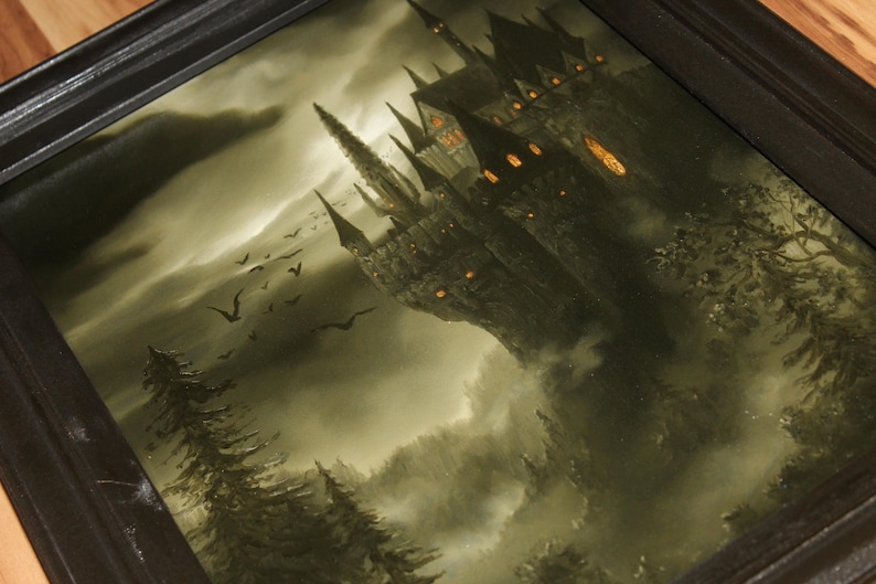 May include: A framed painting depicts a gothic castle perched on a misty cliff, with dark spires and glowing windows. The artwork features a dramatic sky, silhouetted birds, and shadowy trees, creating a mysterious atmosphere.