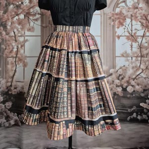 May include: A black button-up shirt and a tiered skirt with a print of stacked books. The skirt has black bands at the top and bottom, creating a unique literary-themed outfit. The outfit is displayed on a mannequin.