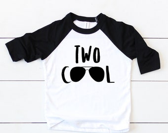 May include: White and black baseball tee shirt with the text "TWO COOL" and a pair of sunglasses graphic.