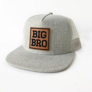 May include: Gray and black trucker hat with a brown leather patch that says "BIG BRO" in black letters.