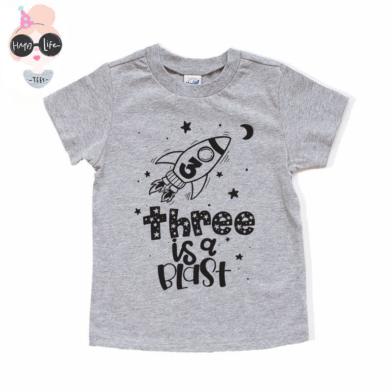 May include: Gray short-sleeved t-shirt with a black rocket ship graphic and the text "Three is a Blast".