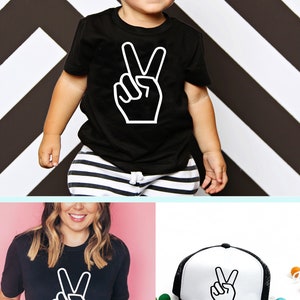 May include: A black t-shirt with a white peace sign graphic. A black and white trucker hat with a white peace sign graphic. The text "HAPPY LIFE PARTIES | PARTY BOXES" is at the bottom of the image. Social media icons and links are included.