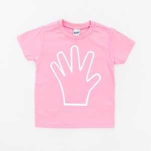 May include: Pink short-sleeved t-shirt with a white outline of a hand on the front.