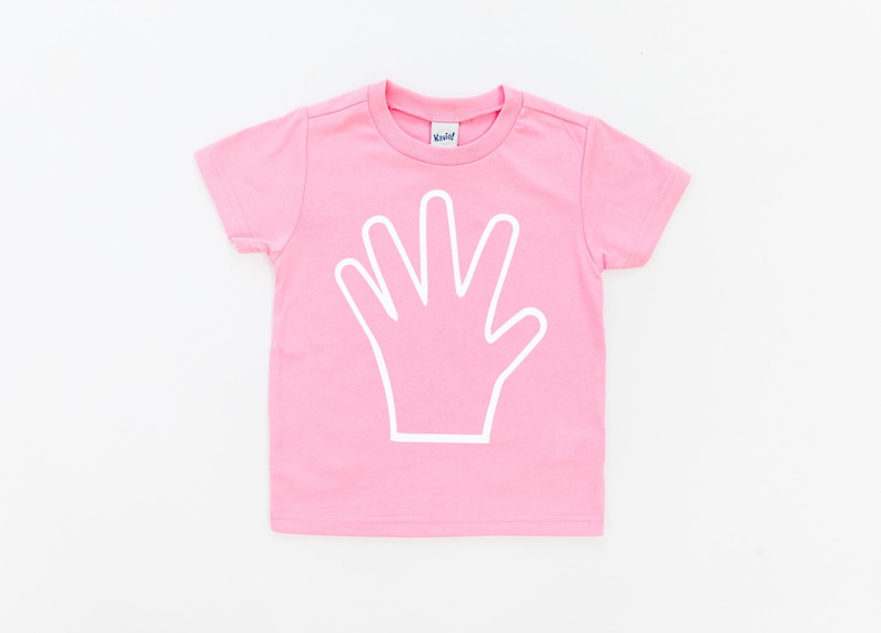 May include: Pink short-sleeved t-shirt with a white outline of a hand on the front.