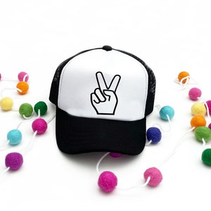 May include: A white and black trucker hat with a peace sign graphic. The hat has a black mesh back and a white front with a black peace sign.