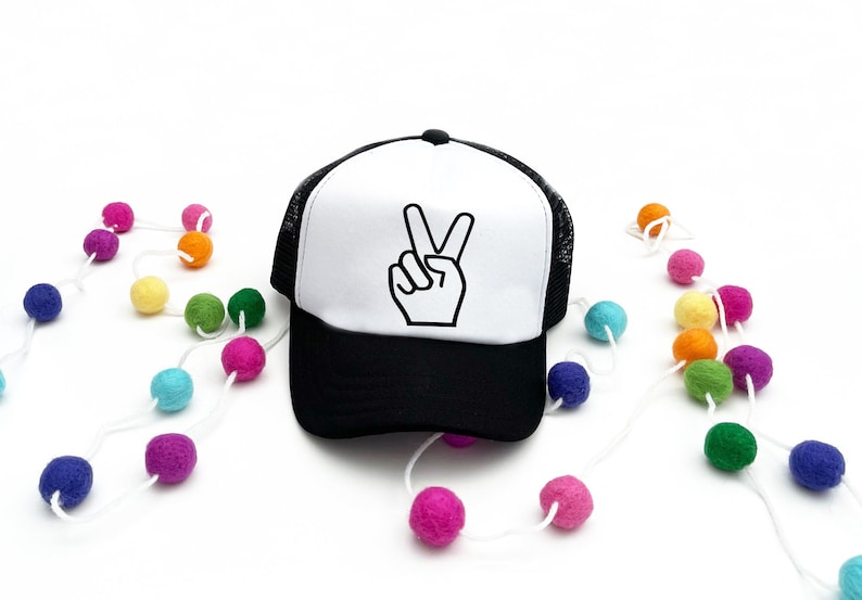 May include: A white and black trucker hat with a peace sign graphic. The hat has a black mesh back and a white front with a black peace sign.