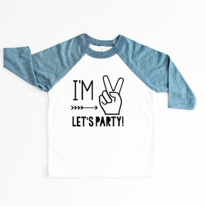 May include: White and blue long-sleeved shirt with a peace sign and the text "I'M LET'S PARTY!" printed on the front.