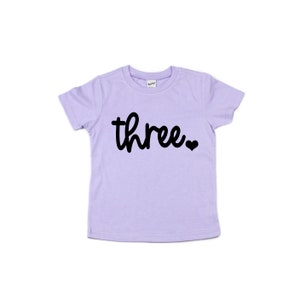 Puede incluir: Camiseta lila claro para ni&ntilde;os peque&ntilde;os con la palabra "three" en escritura negra, seguida de un peque&ntilde;o coraz&oacute;n negro. La camiseta est&aacute; hecha de material suave y est&aacute; dise&ntilde;ada para el tercer cumplea&ntilde;os de un ni&ntilde;o.