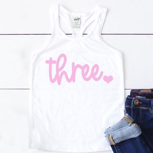 Puede incluir: Camiseta blanca de tirantes con un 'tres' rosa y un coraz&oacute;n rosa en la parte delantera.