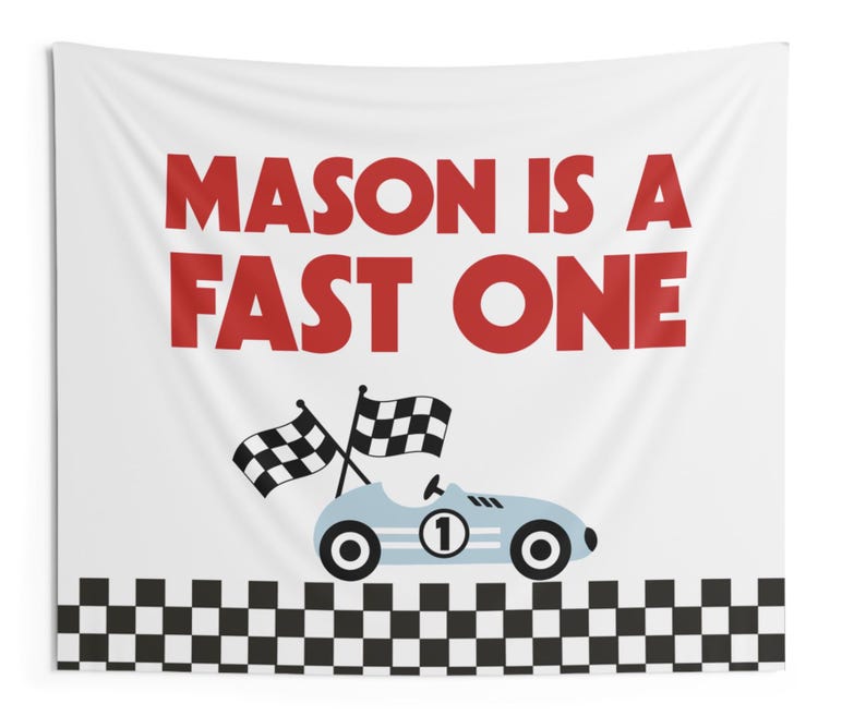 May include: White fabric wall hanging with the text "MASON IS A FAST ONE" in red. A light blue race car with the number 1 and checkered flags is featured below the text. A black and white checkered pattern borders the bottom.