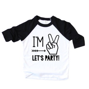 May include: A white and black baseball tee shirt with a black and white graphic that says "I'm 2 Let's Party!" with a peace sign and an arrow.