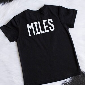 May include: Black t-shirt with the word "MILES" printed in white on the back.