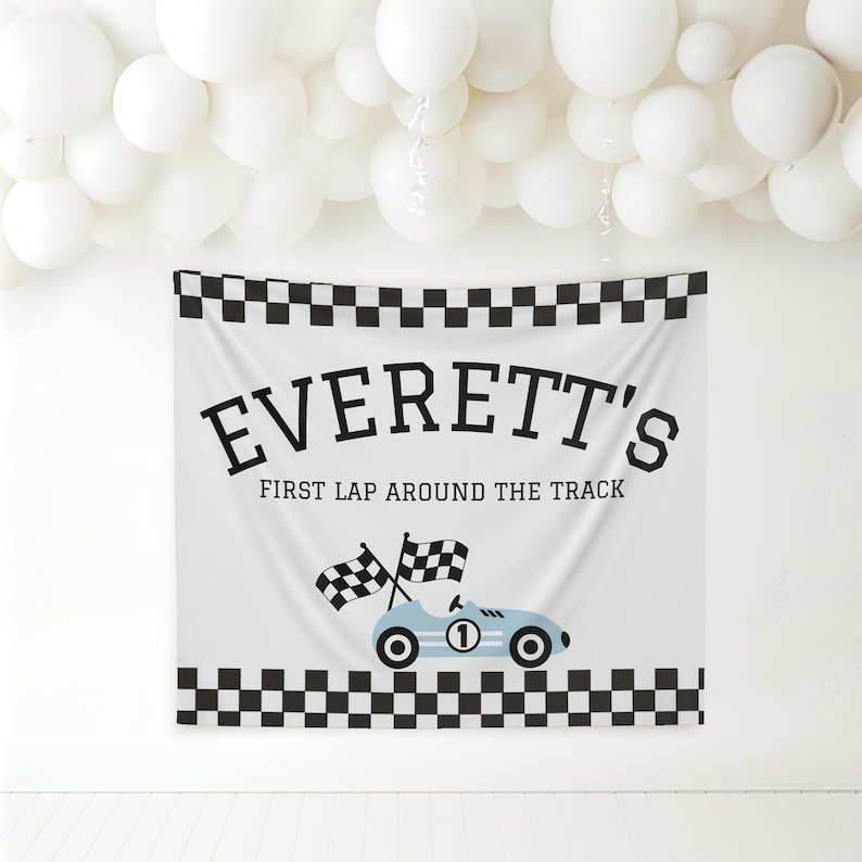 May include: White banner with black checkered borders and the text "EVERETT'S FIRST LAP AROUND THE TRACK". A light blue race car with the number 1 and checkered flags is featured below the text. White balloons are in the background.