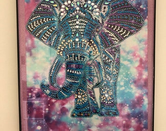 May include: A framed diamond painting of an elephant with a blue, purple, and white patterned design on a galaxy background.