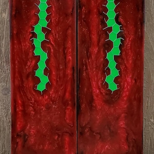 May include: Two rectangular blocks with a deep red, swirling pattern. A vertical line of green, interconnected hexagonal shapes runs down the center of each block. The blocks have a glossy finish and are set against a wooden background.