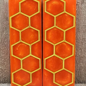 May include: Two rectangular orange resin blocks with a yellow honeycomb design. The resin has a swirled, textured appearance. The honeycomb pattern is outlined in bright yellow, creating a striking contrast against the orange background. The blocks are displayed vertically.