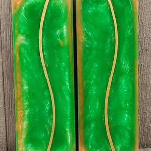 May include: Two rectangular resin pieces with a vibrant green interior and gold-toned edges. A thin, curved, gold-colored line runs through the center of each piece. The pieces are displayed against a wooden background.