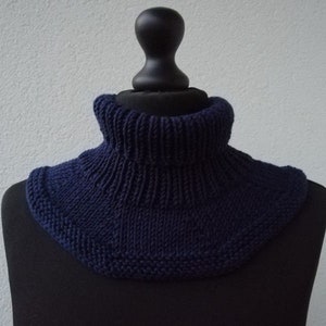 Könnte beinhalten: Ein marineblauer gestrickter Halsschmuck oder Schal, getragen auf einer schwarzen Puppe.