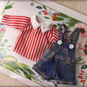 May include: Miniature doll clothing set featuring a red and white striped shirt with a white collar and denim overalls with white buttons. The clothing is displayed on a floral patterned background.