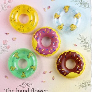 May include: Five inflatable pool floats in the shape of donuts and rings. The rings are yellow, green, and clear with duck patterns. The donut floats are pink and brown with sprinkles. The text "The hand flower" is at the bottom.