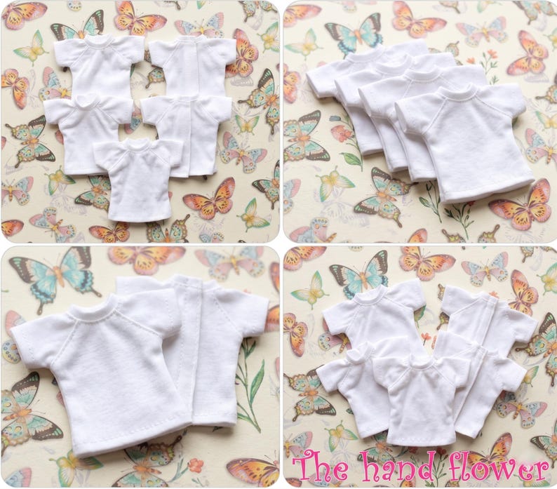 May include: Multiple white doll-sized t-shirts with short sleeves are arranged on a butterfly-patterned background. The shirts are made of a soft fabric and are neatly displayed, showcasing their simple design.