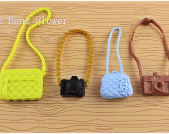 May include: Four miniature accessories: a lime green quilted purse, a black camera, a light blue purse, and a brown camera. Each has a strap or chain. The text "The Hand Flower" is in the upper left corner.