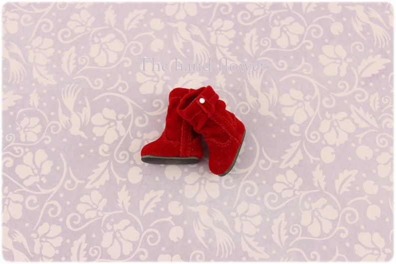 Puede incluir: Un par de botas de ante rojo con un dobladillo y un peque&ntilde;o bot&oacute;n blanco. Las botas est&aacute;n sobre un fondo blanco con un patr&oacute;n floral.