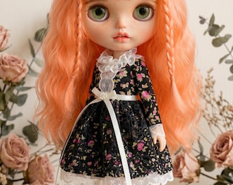 May include: A doll with orange hair styled in braids and long waves, wearing a black floral dress with white lace trim and a white ribbon belt. The doll has green eyes and is wearing black shoes and white socks. The text "The hand flower" is at the bottom.