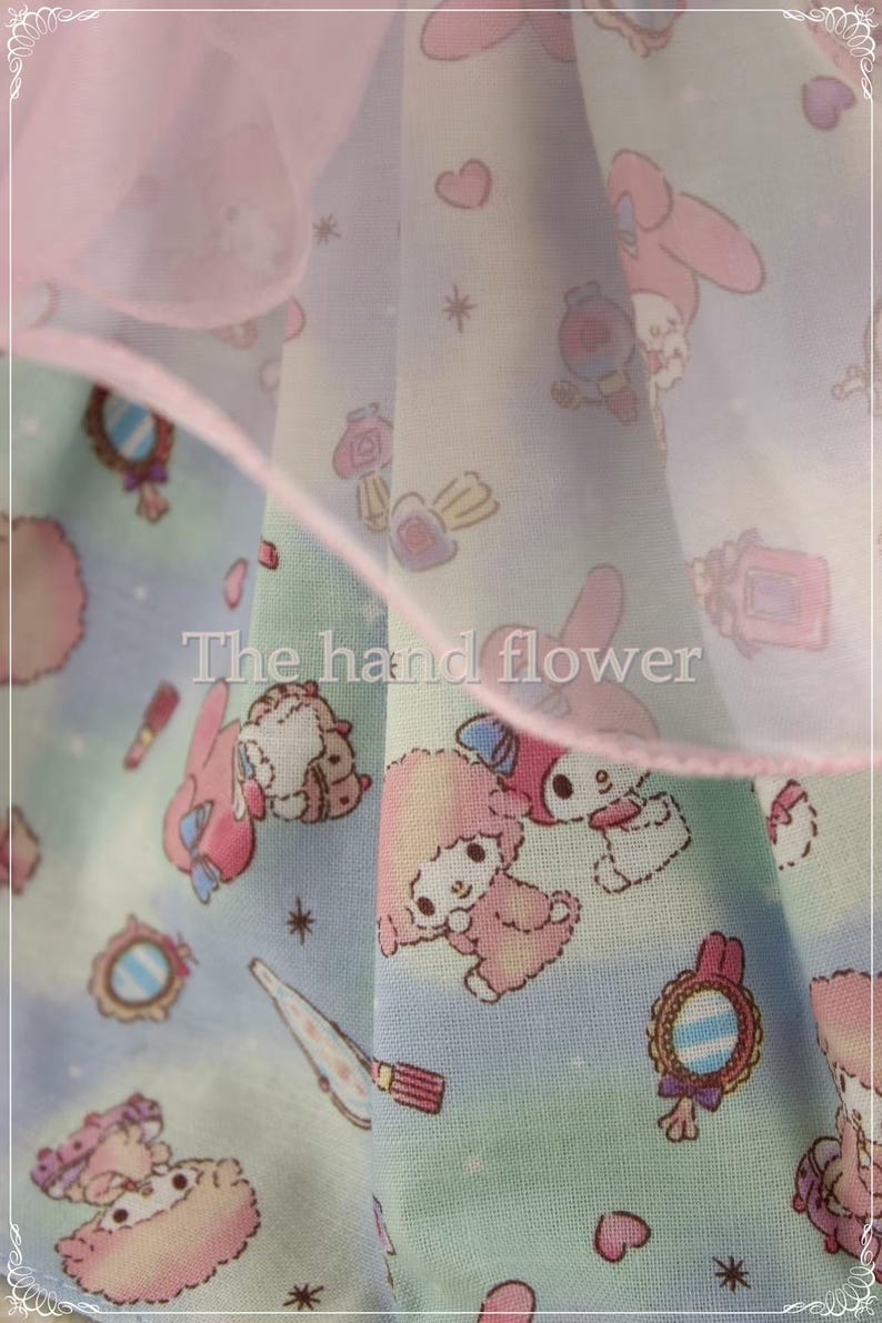 May include: A light blue fabric with a repeating pattern of cartoon characters, mirrors, and makeup items. The fabric has a pink ruffle trim and the text "The hand flower".