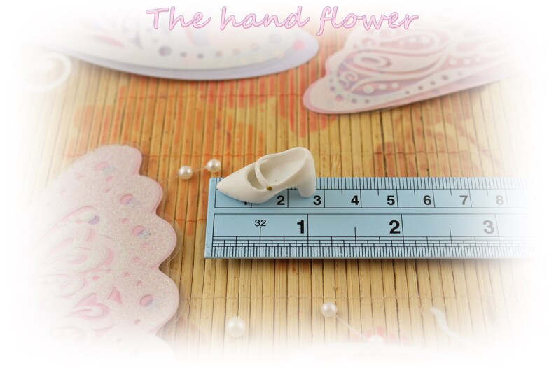 May include: A white ceramic shoe with a gold buckle, measuring approximately 1 inch in length, is placed on a blue ruler with black markings.