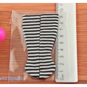 May include: A pair of black and white striped knee-high socks for a doll. The socks are approximately 6 cm long.