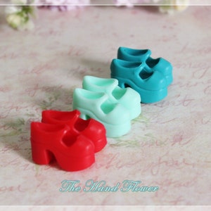 以下が含まれることがあります： 赤、ターコイズ、ライトブルーの3組のミニチュアプラットフォームシューズ。靴はプラスチック製で、太いヒールが付いています。