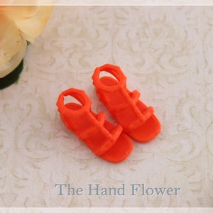 May include: A pair of bright orange gladiator sandals with straps and buckles. The sandals are made of plastic and have a simple design.