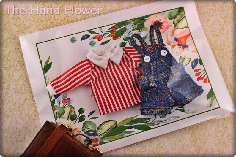 May include: Miniature doll clothing set featuring a red and white striped shirt with a white collar and cuffs, and denim overalls with white buttons. The set is displayed on a floral patterned background with the text "The Hand Flower".