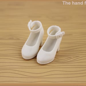 May include: A pair of white doll shoes with ankle straps. The shoes have a small heel and are made of a smooth plastic.