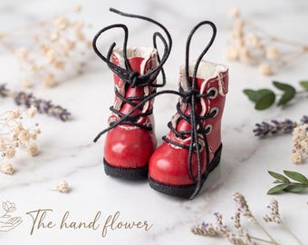 May include: Miniature red boots with black laces and white trim. The boots have a black sole. The image includes dried flowers and the text "The hand flower".