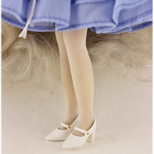 May include: White doll shoes with a gold buckle and a white fishnet stocking on the doll's leg. The doll is wearing a light blue dress.