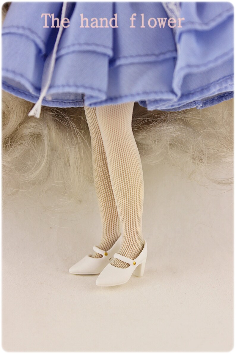 May include: White doll shoes with a gold buckle and a white fishnet stocking on the doll's leg. The doll is wearing a light blue dress.